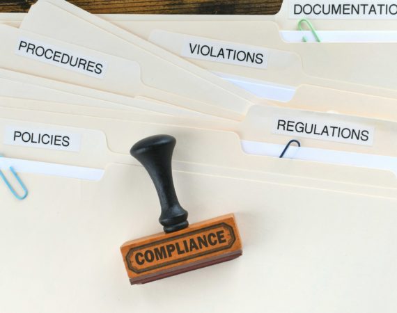 Compliance rubber stamp on folders marked Policies Regulations Violations Procedures Documentation.